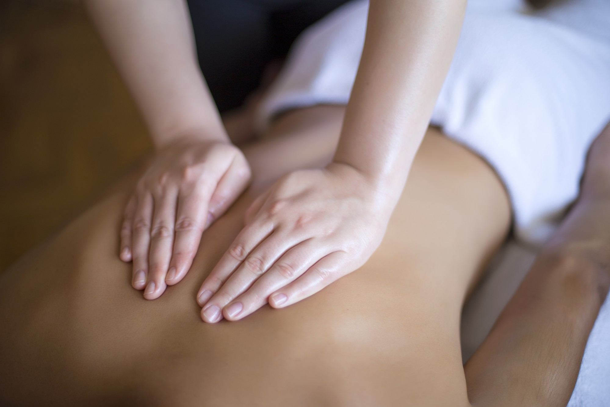 A female chiropractor pushing on a male patients back from above, cupping her hands