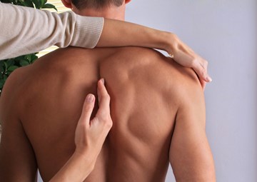 A female chiropractor working on a male patients back while he stands looking away from her