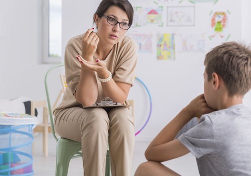 A female psychologist talking to a young male patient in a white room decorated in children drawings