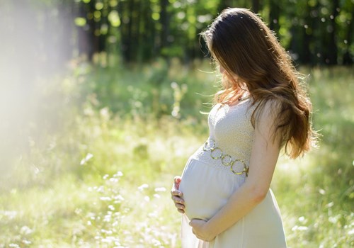 A pregnant woman wearing a white dress who is standing in a field