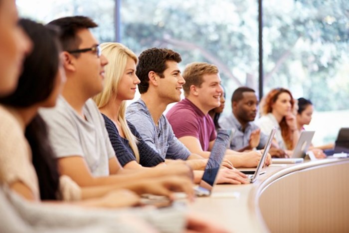 A group of students looking at something while taking notes on their laptops