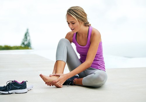 A woman sitting on the ground clutching her right foot in pain