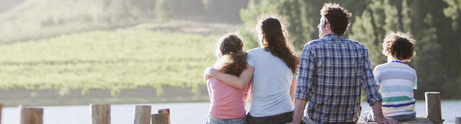 A family of four sitting on a pier, looking out at the sunset