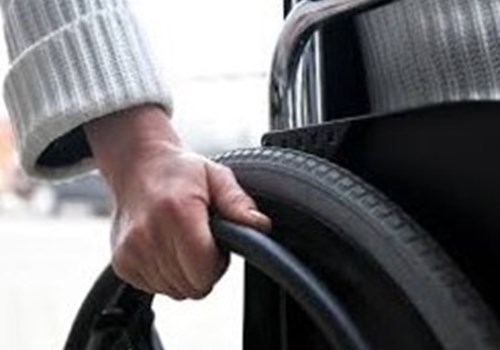 A person siting in a wheelchair with their hand placed firmly on the right wheel